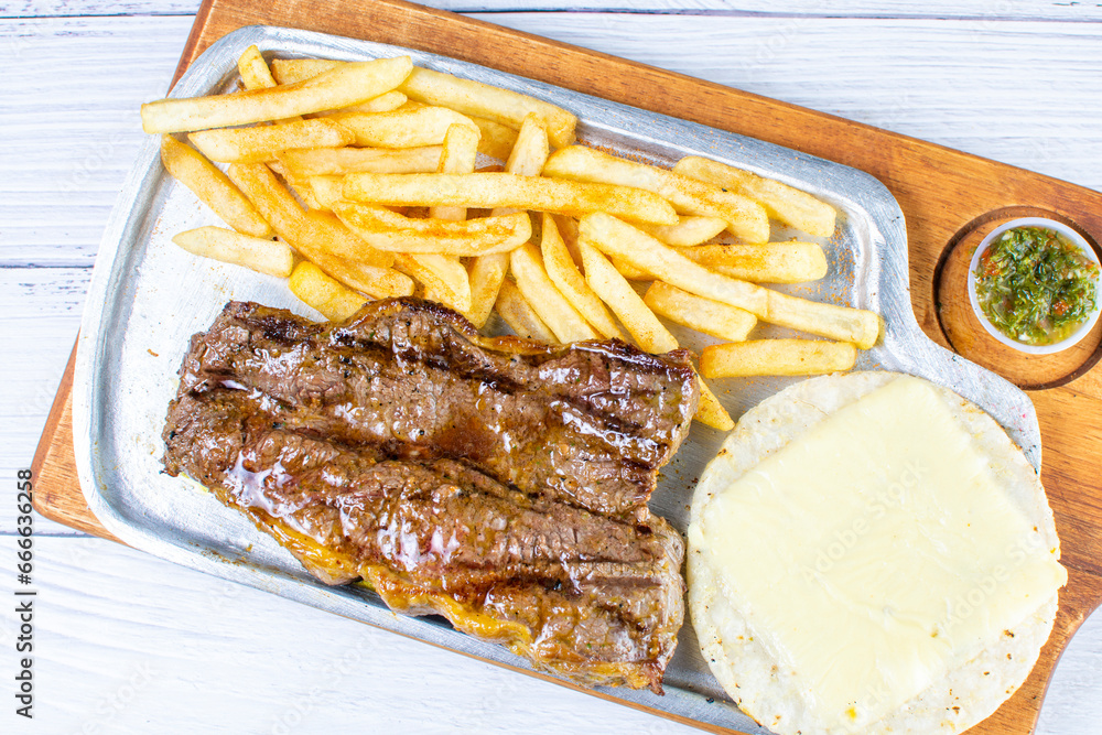 Tray of roasted haunch tip, accompanied by arepa with cheese, French fries and chimichurri