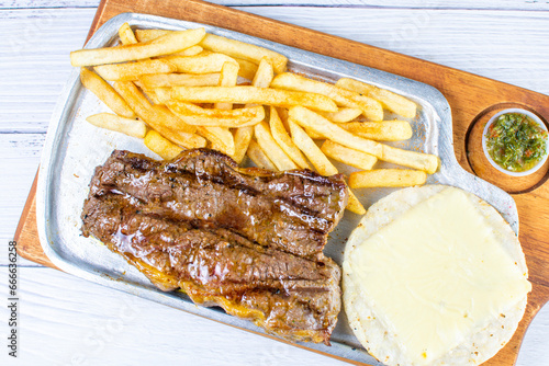 Slika na platnu Tray of roasted haunch tip, accompanied by arepa with cheese, French fries and c