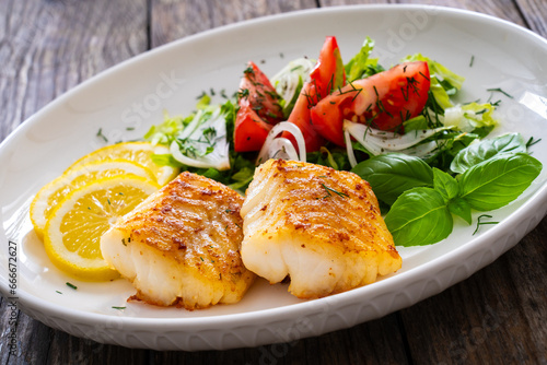 Seared cod loin and fresh vegetables on wooden table
