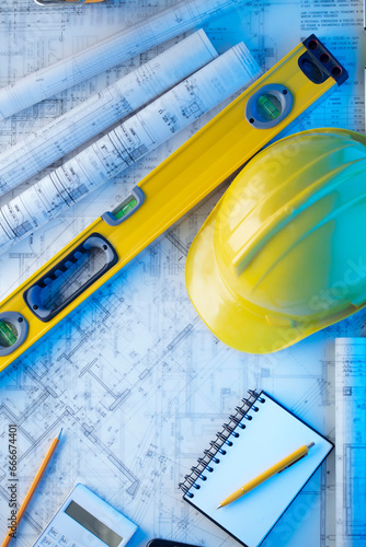 Architect and contractor concept. Rolls with projects. Tool kit of the contractor: yellow hardhat, libella and notebook. 
