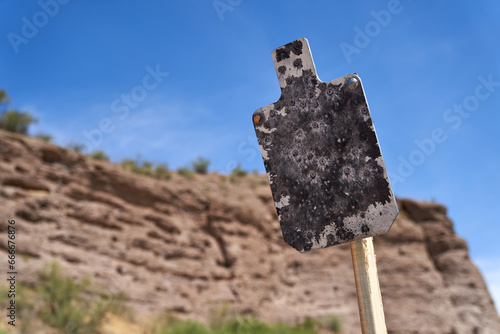 Weathered tactical AR500 Steel silhouette targets with sitting on wood stands at desert outdoor range in summer.
