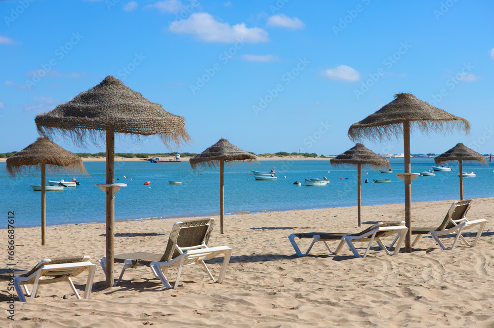 Straw umbrellas and sun loungers on the beach on a sunny day. The concept of rest and relaxation, holidays and travel. In the background the fishermen's boats.