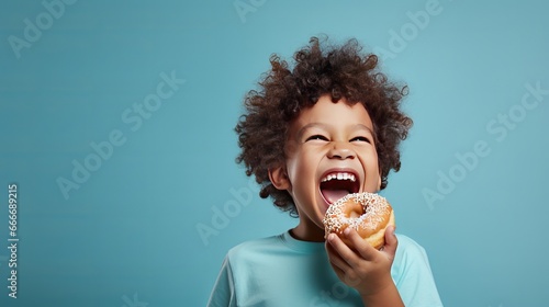 Fotografia A little boy with a smile is eating a donut on a blue background wall