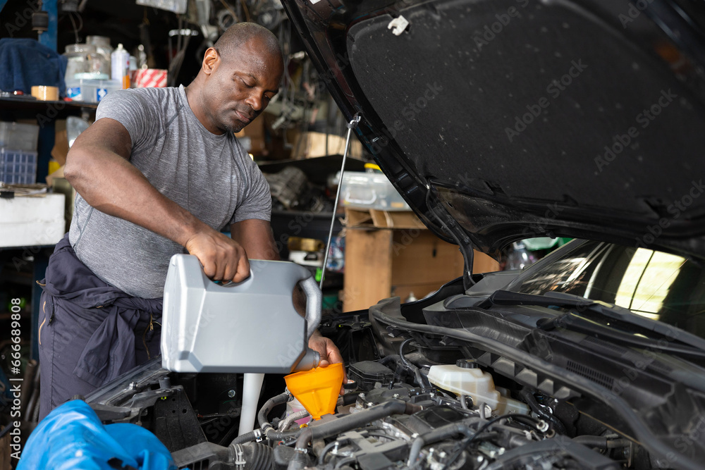 African mechanic worker filling engine oil into a car in garage African mechanic worker filling engine oil into a car in garage