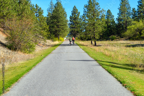 Two bicyclists ride their bikes along the Centennial Trail near the Idaho Washington border in the rural city of Post Falls, Idaho, a suburb of the Spokane and Coeur d'alene general areas.