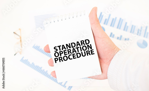 Businessman holding a white notepad with text STANDARD OPERATION PROCEDURE, business concept