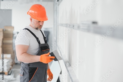man drywall worker or plasterer putting mesh tape for plasterboard on a wall using a spatula and plaster. Wearing white hardhat, work gloves and safety glasses. Image with copy space. photo