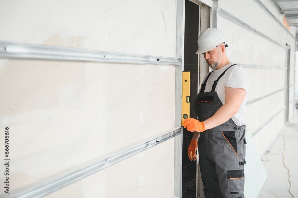 man drywall worker or plasterer putting mesh tape for plasterboard on a wall using a spatula and plaster. Wearing white hardhat, work gloves and safety glasses. Image with copy space. man drywall worker or plasterer putting mesh tape for plasterboard on a wall using a spatula and plaster. Wearing white hardhat, work gloves and safety glasses. Image with copy space.