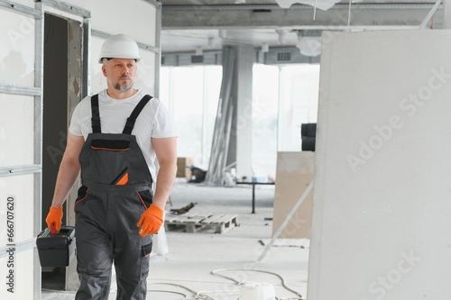 Portrait of a builder in working uniform with protective helmet standing with instruments at the construction site indoors