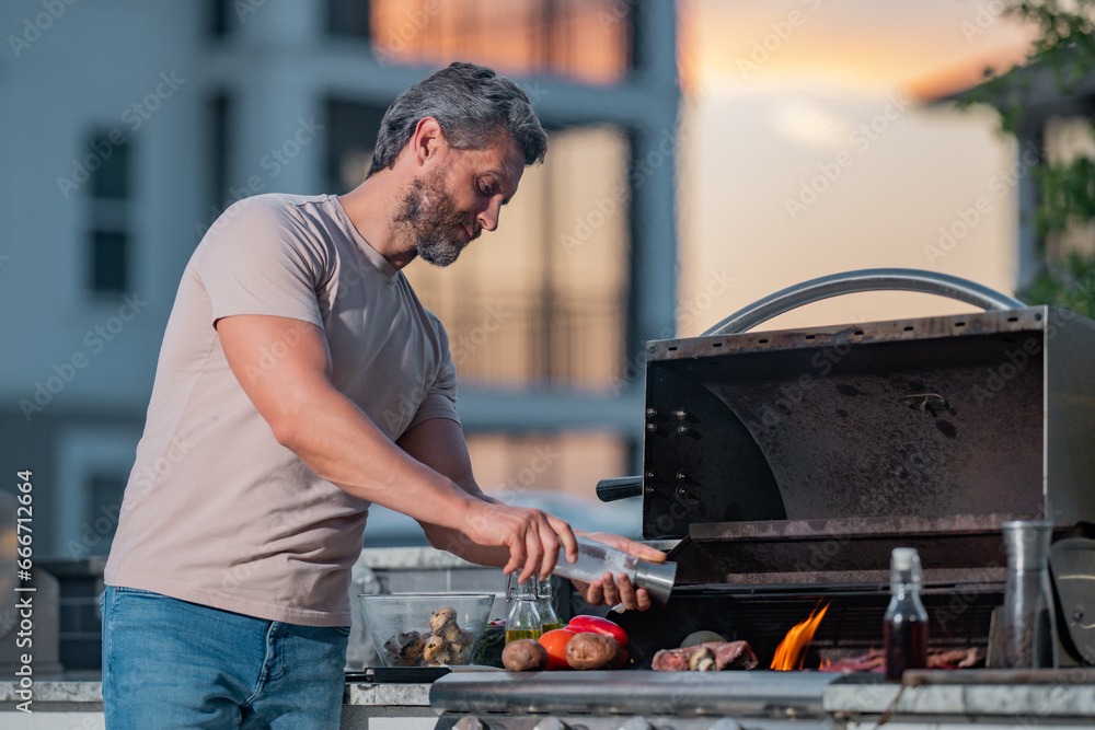 Handsome man preparing barbecue. Male cook cooking meat on barbecue grill. Guy cooking meat on barbecue for summer family dinner at the backyard of the house.