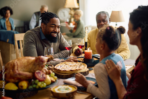Happy black father talks to his daughter during Thanksgiving family meal at dining table.