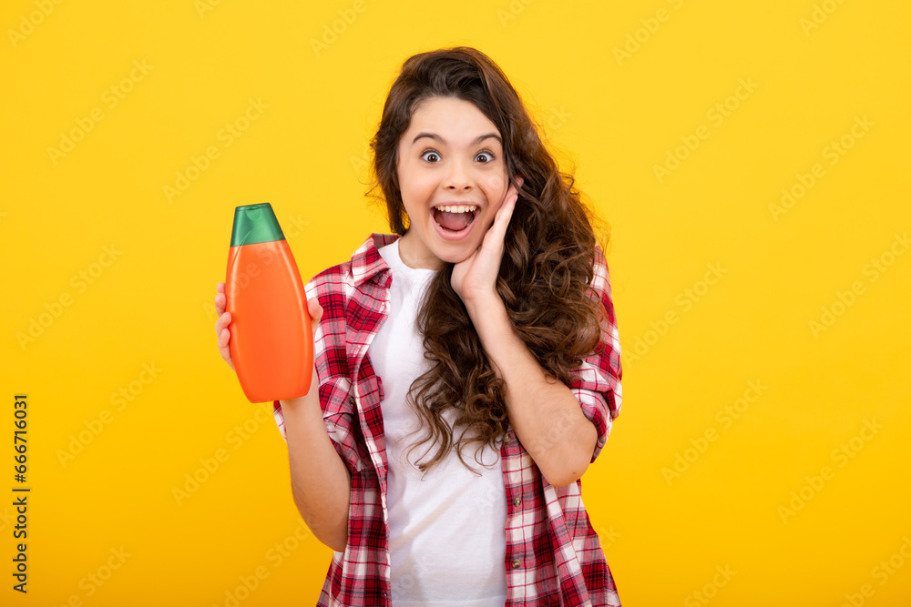 Amazed teenager. Teenager child girl showing bottle shampoo conditioners or shower gel isolated on yellow background. Hair cosmetic product. Mock up bottle. Excited teen girl. Amazed teenager. Teenager child girl showing bottle shampoo conditioners or shower gel isolated on yellow background. Hair cosmetic product. Mock up bottle. Excited teen girl.
