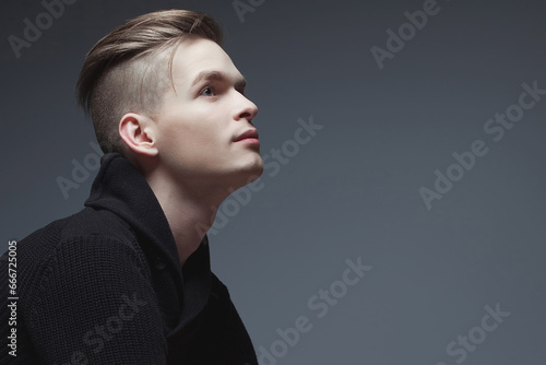 Male beauty concept. Fashionable young man with stylish haircut wearing trendy black sweater, posing over gray background. Perfect hair, skin. Hipster style. Copy-space. Close up. Studio shot