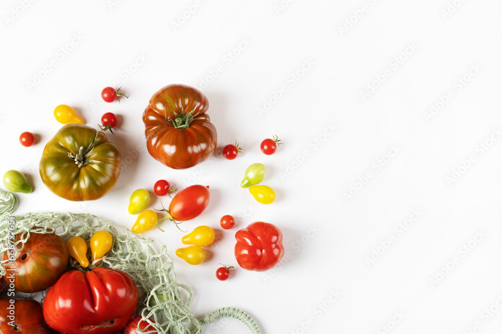 Red, green, yellow and striped tomatoes in a string bag on a gray table with space for text. Flat lay. Healthy food, fresh healthy vegetables from the garden
