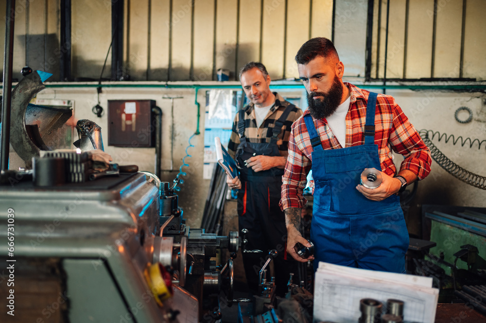 Two metallurgists looking at a lathe machine in a metalwork factory. Two metallurgists looking at a lathe machine in a metalwork factory.