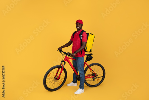 Wallpaper Mural Positive confident millennial black man courier in uniform with backpack rides on bike Torontodigital.ca