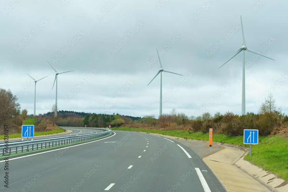Wind turbines stand along the road against the background of clouds.