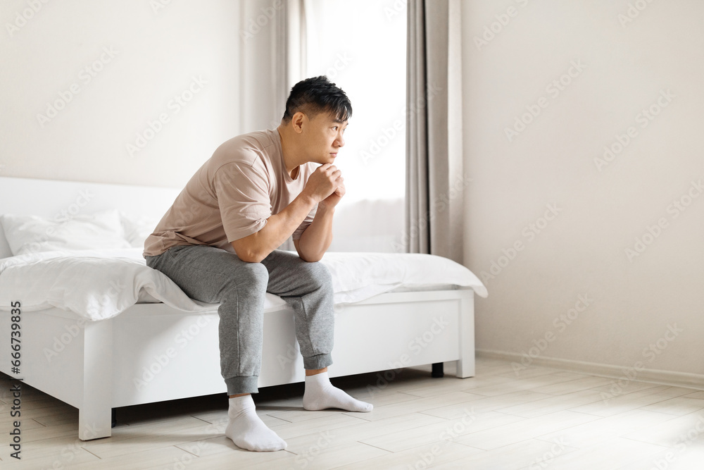 Depressed mature korean man sitting on bed in the morning Depressed mature korean man sitting on bed in the morning