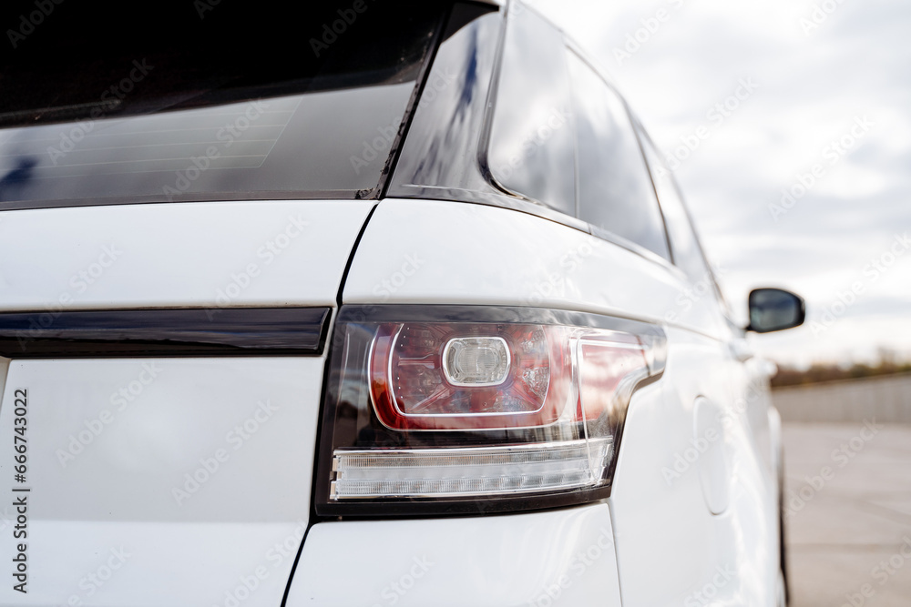Obraz premium Glass headlight at the rear of the car, parking lights, red brake light, part of the car rear view, white body color.