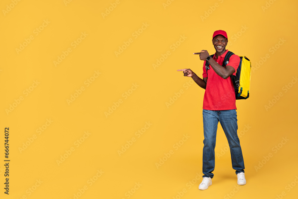 Glad millennial black guy courier in uniform with big backpack point finger at copy space Glad millennial black guy courier in uniform with big backpack point finger at copy space