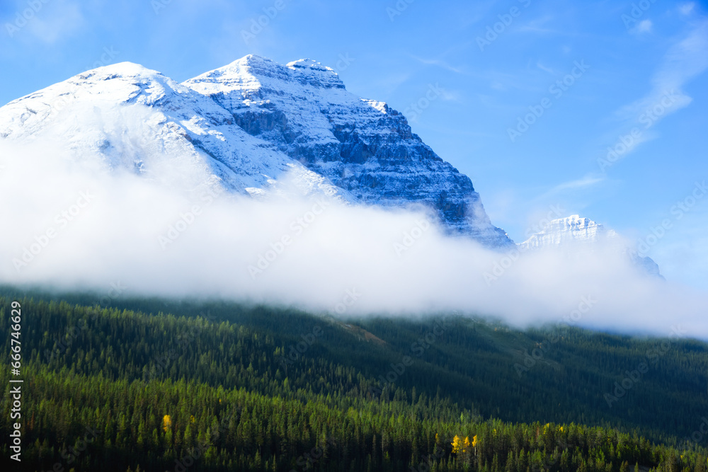 Mountain with white peak and cloud around among green forest.