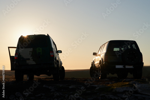 Two passenger cars on top of a mountain at dawn in the first rays of the rising sun.