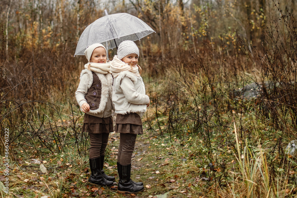 Portrait of young twin girls standing under an umbrella in the park, looking at the camera.