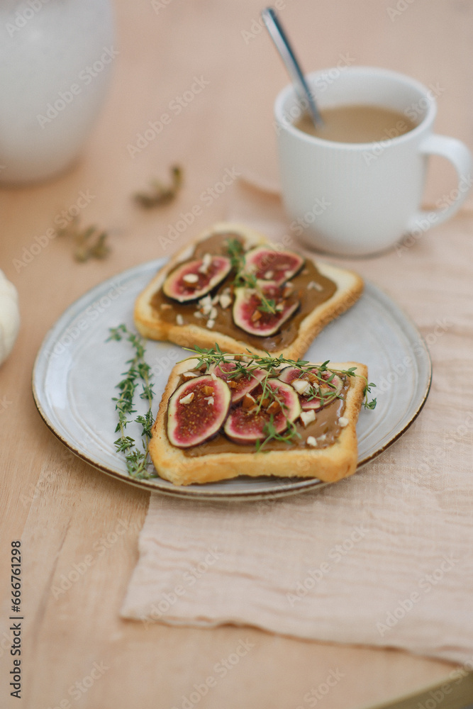 Home autumn breakfast, two toasts with almond butter, figs, coffee, pumpkins, candle on a round wooden table. Home autumn breakfast, two toasts with almond butter, figs, coffee, pumpkins, candle on a round wooden table.