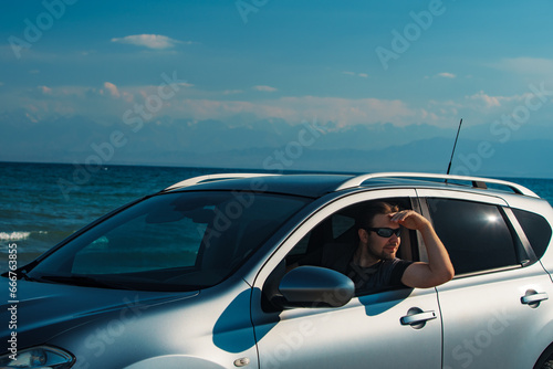 Handsome young man in sunglasses driving car on seashore at summer day © chaossart