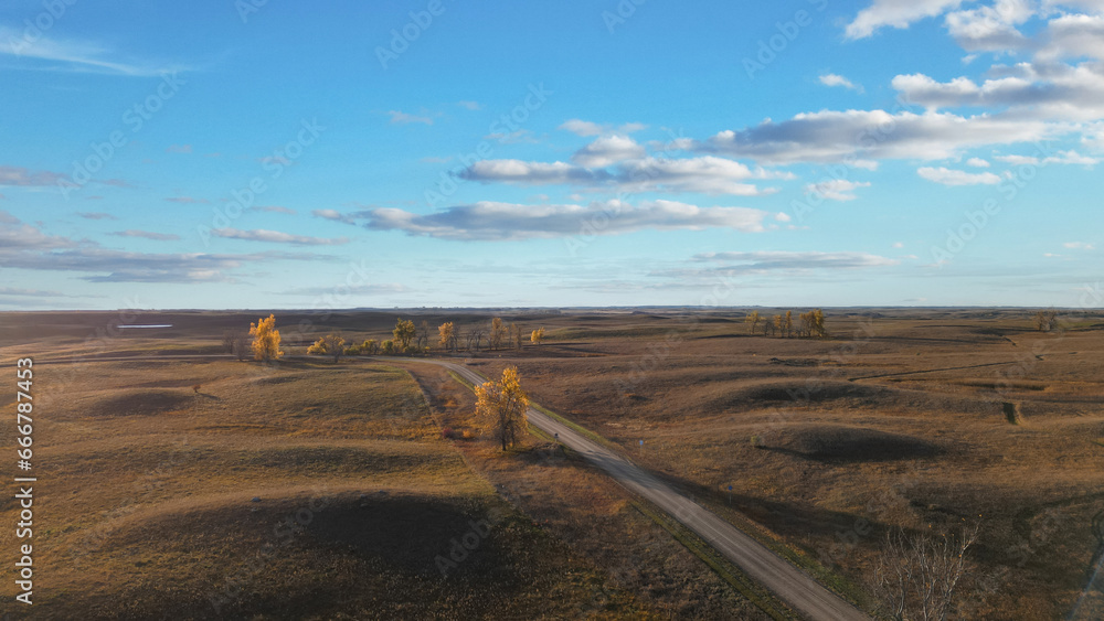Autumn hills with rural road going through and beautiful sky with clouds. Drone photography of a view of the evening horizon and sunset. USA Midwest landscape. South Dakota in fall colors.