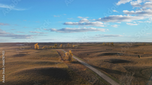 Autumn hills with rural road going through and beautiful sky with clouds. Drone photography of a view of the evening horizon and sunset. USA Midwest landscape. South Dakota in fall colors.