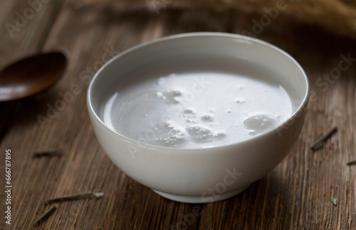 Coconut milk in a bowl on a wooden table. Dry grass and a spoon lie nearby