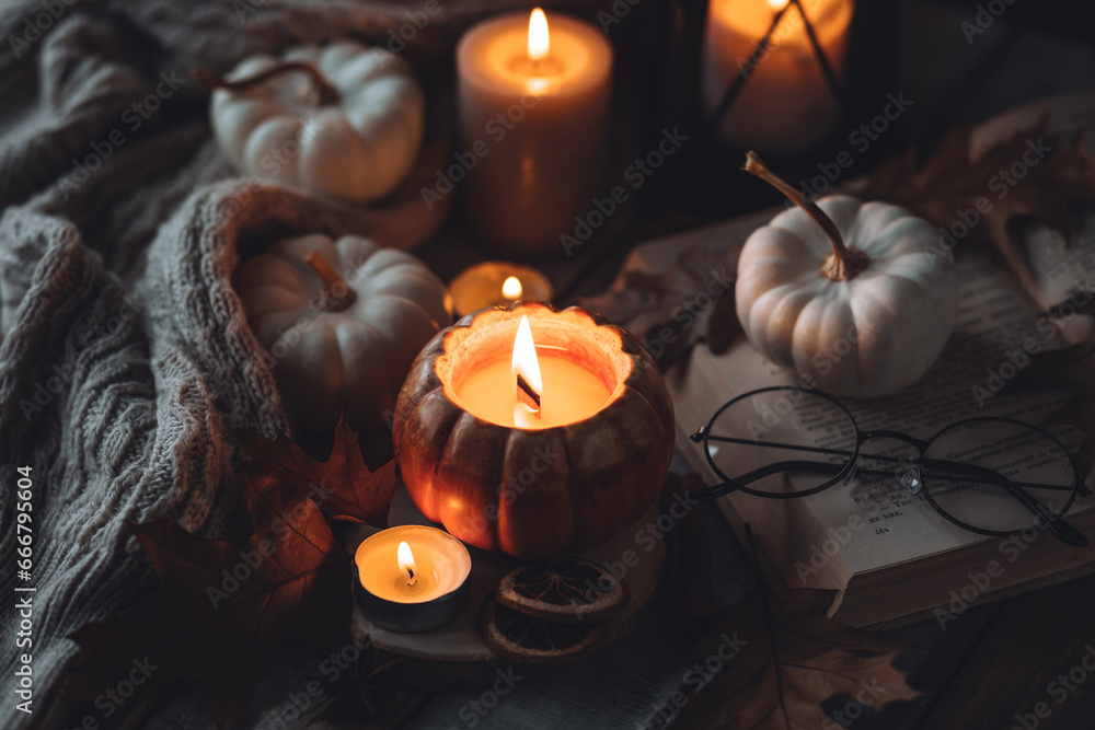 Atmospheric candle - shape of pumpkins, autumn decor, book on grey fall rainy day. Autumn cozy home atmosphere, inspiration, hygge concept. Aromatherapy, warming, relaxation. Wooden background