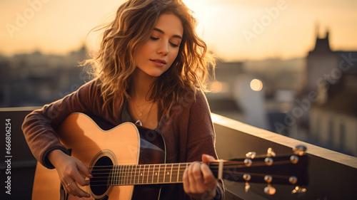 Adult girl plays guitar on building roof at sunset, young woman guitarist practices music. Player with acoustic instrument outside home. Concept of summer, city, musician photo