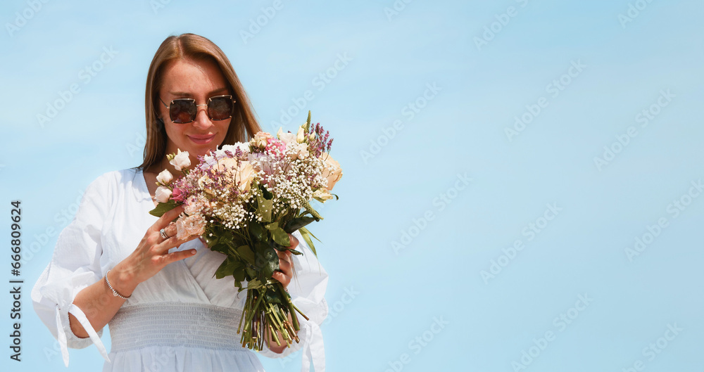 Joyful Young Woman Holding a Bouquet of Flowers on a Beach with Blue Sky Background