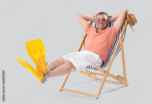 Mature man with flippers relaxing in deck chair on light background
