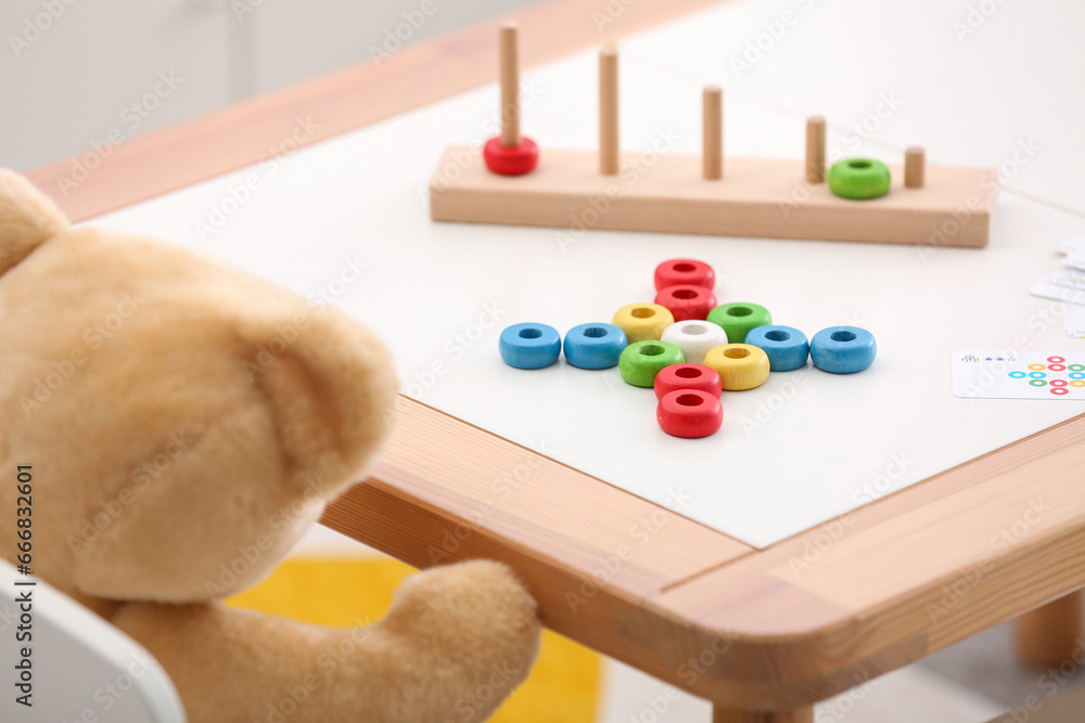 Stacking and counting game on table and teddy bear indoors, closeup. Educational toy for motor skills development Stacking and counting game on table and teddy bear indoors, closeup. Educational toy for motor skills development