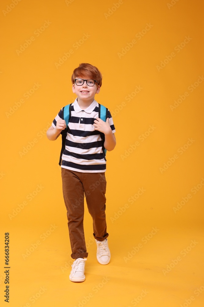 Naklejka premium Happy schoolboy in glasses on orange background