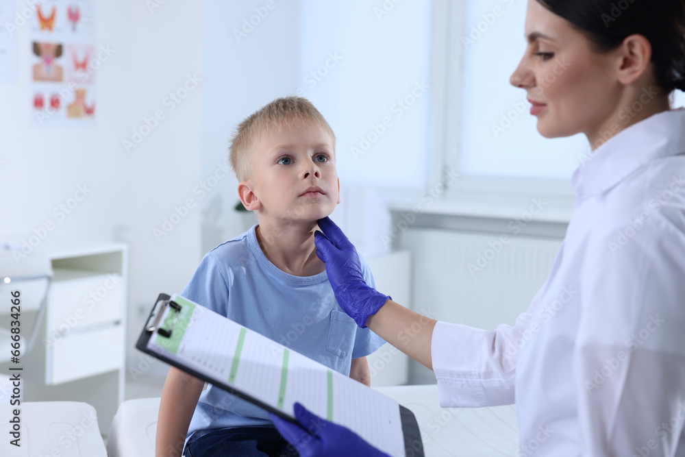 Endocrinologist with clipboard examining boy's thyroid gland at hospital Endocrinologist with clipboard examining boy's thyroid gland at hospital