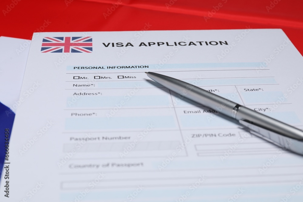 Immigration to United Kingdom. Visa application form and pen on flag, closeup Immigration to United Kingdom. Visa application form and pen on flag, closeup
