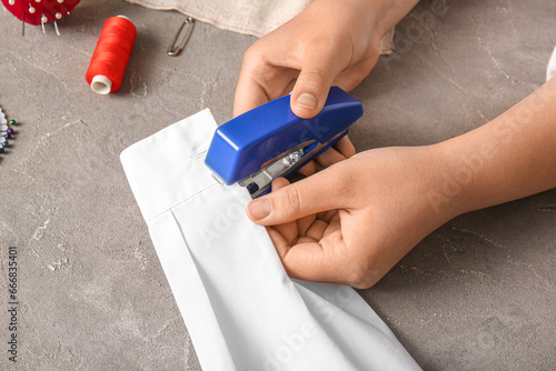 Female hands with different supplies sewing blouse on grunge grey background