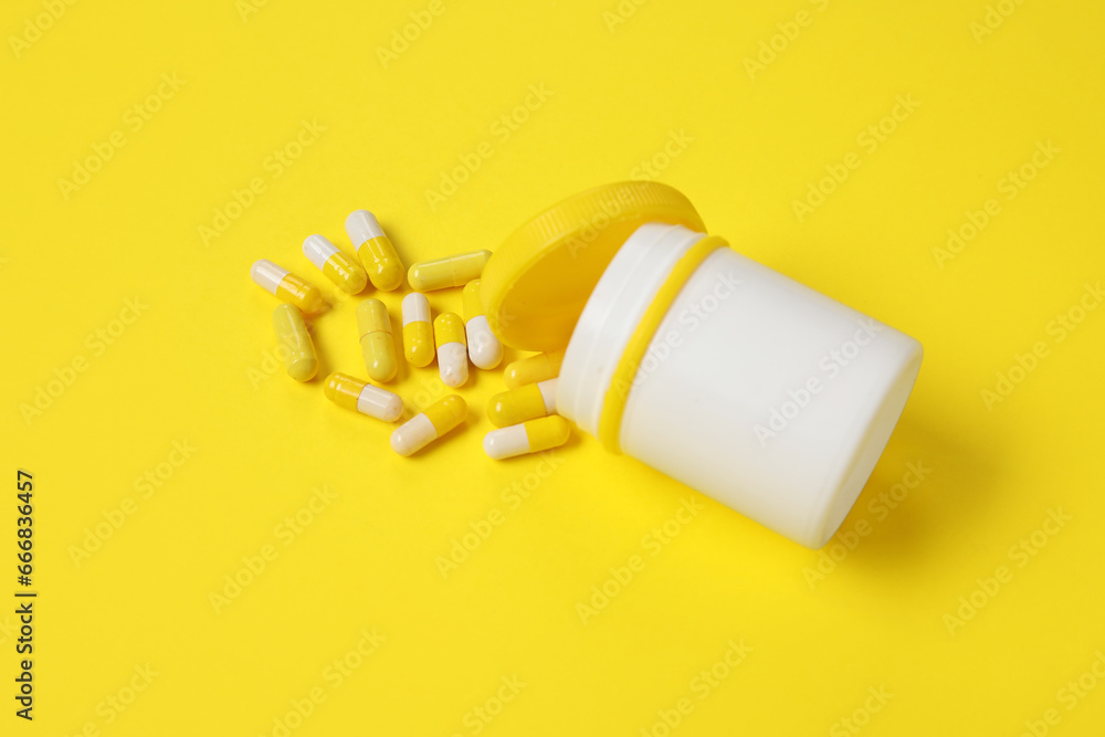 Jar with scattered pills on yellow background Jar with scattered pills on yellow background