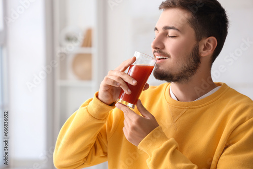 Young man drinking tomato juice at home, closeup