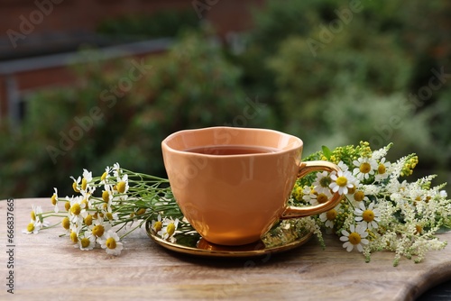 Cup of delicious chamomile tea and fresh flowers outdoors