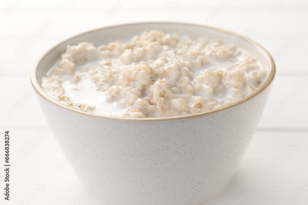 Tasty boiled oatmeal in bowl on white table, closeup Tasty boiled oatmeal in bowl on white table, closeup