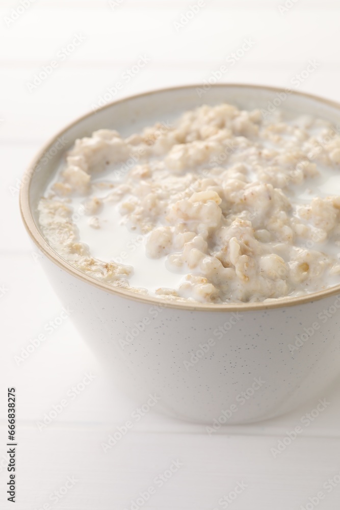 Tasty boiled oatmeal in bowl on white table, closeup Tasty boiled oatmeal in bowl on white table, closeup