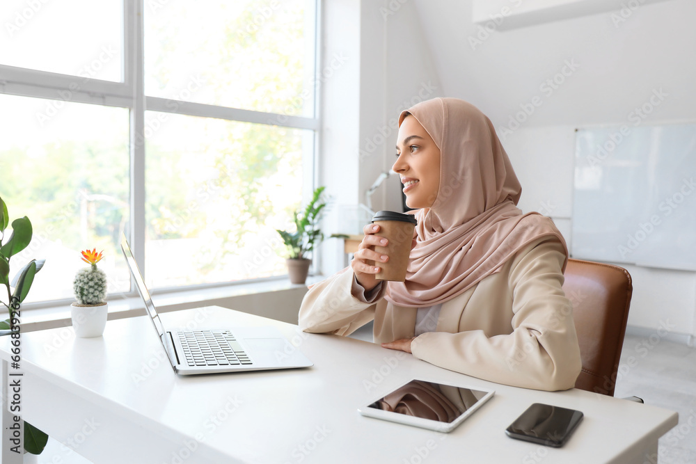 Pretty Muslim female programmer with cup of coffee working in office Pretty Muslim female programmer with cup of coffee working in office