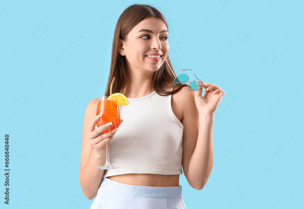 Beautiful young woman with glass of tasty aperol spritz cocktail on blue background Beautiful young woman with glass of tasty aperol spritz cocktail on blue background