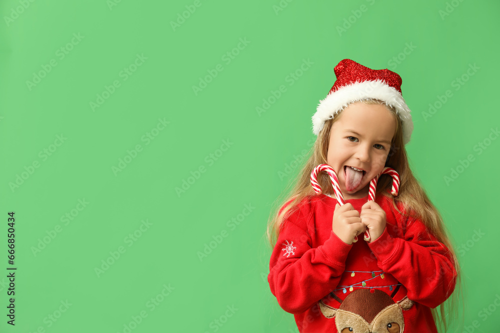 Cute little girl in elf costume with candy canes on green background Cute little girl in elf costume with candy canes on green background