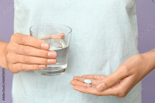 Woman with pills and glass of water on lilac background, closeup